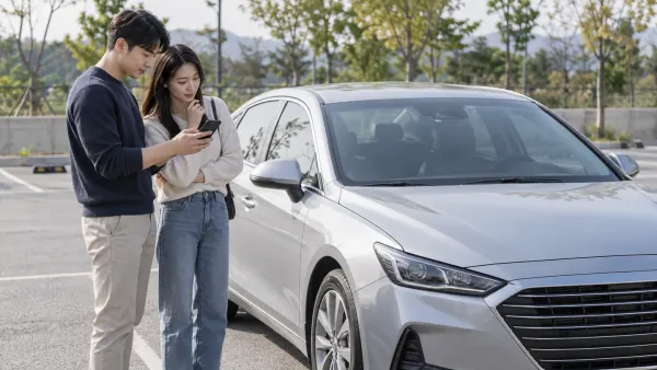 은색 차량 옆에서 휴대전화 화면과 차량을 함께 살펴보는 두 성인